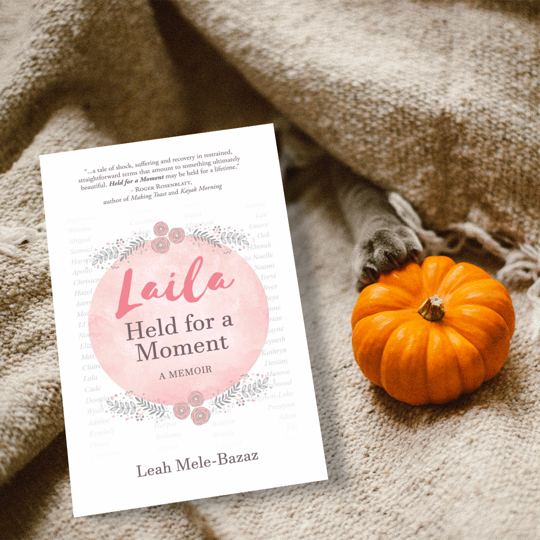 a book with the title "Laila: Held for a Moment" by Leah Mele-Bazaz sitting beside a small orange pumpkin