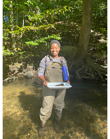 Akilah Chatman stands in a creek, holding a tray of specimens