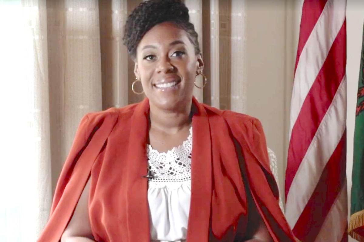 Alexandra J. King Pile smiles during a video. An American flag sits behind her.