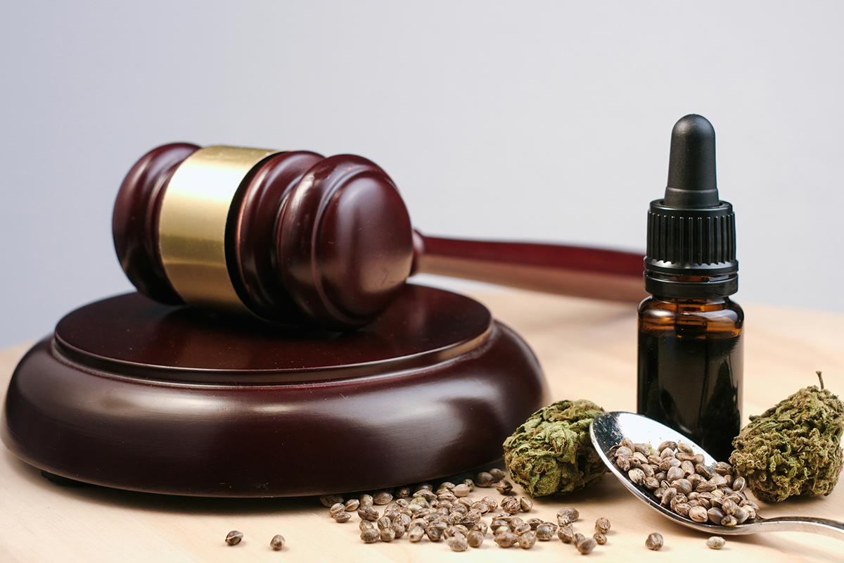 a wooden gavel sits beside a tincture and loose marijuana, representing the legal system's control over the substance