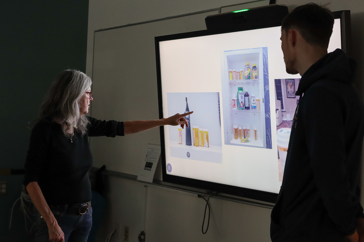 A photography professor and student stand in front of a projected image. The professor points to the photo and critiques it.