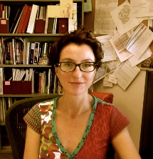 Headshot of Martinez-Donate wearing glasses in office with bookshelf and crowded bulletin board in background.