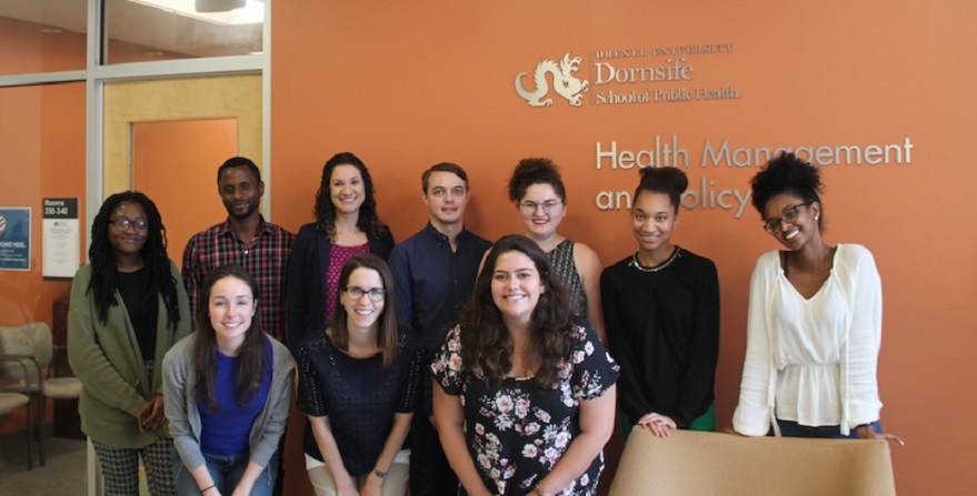 MPH students stand in front of Health Management and Policy logo