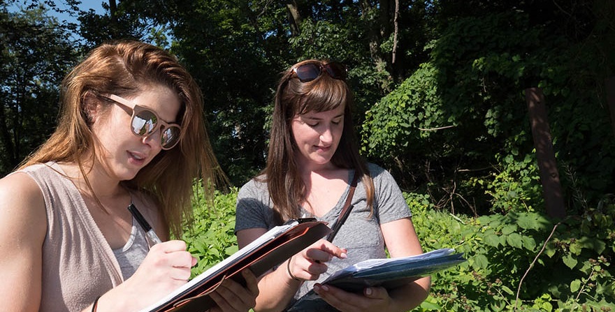 two students in a park with clipboards