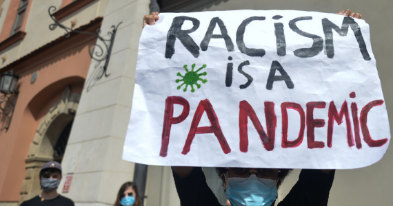 Woman holding sign "racism is a pandemic!"