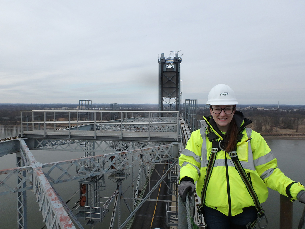 Danielle Schroeder stands on top of a bridge in a yellow safety jacket and hard hat.