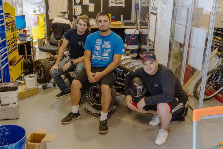 Three young men pose on a go-kart