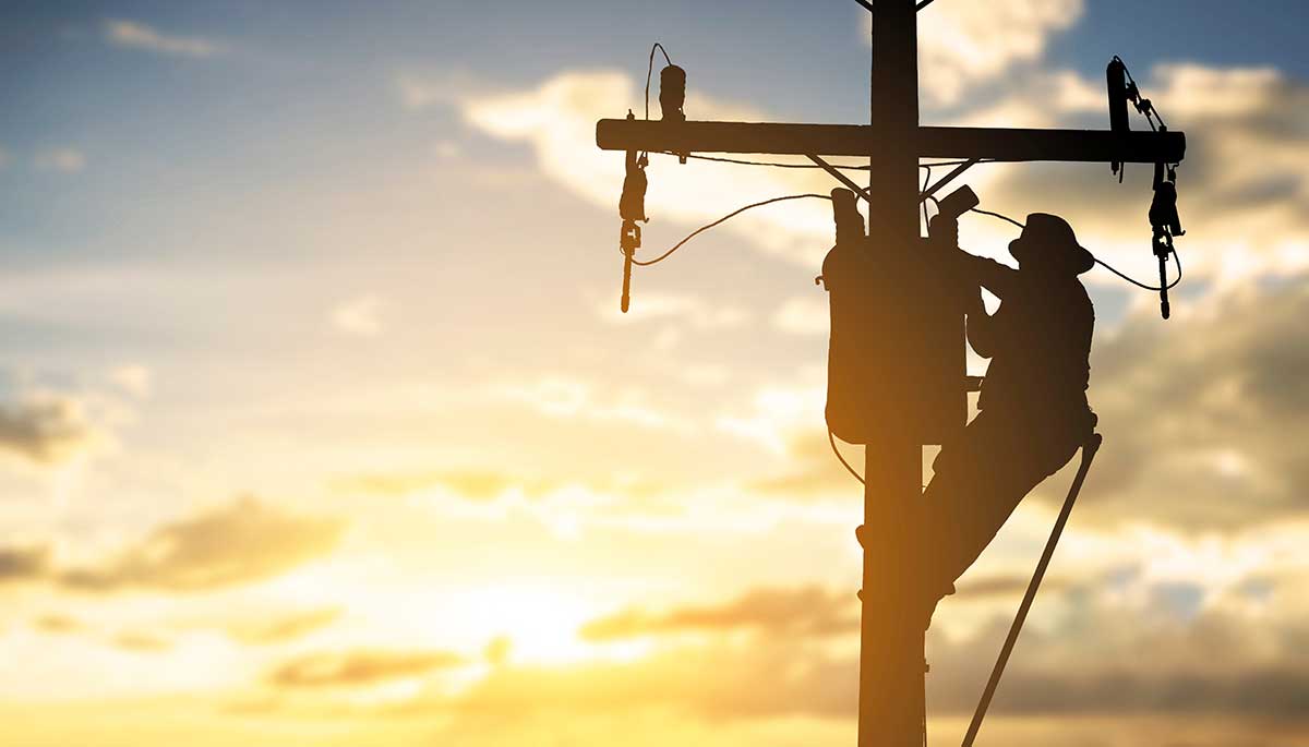 electrician on a telephone pole with sunset in background
