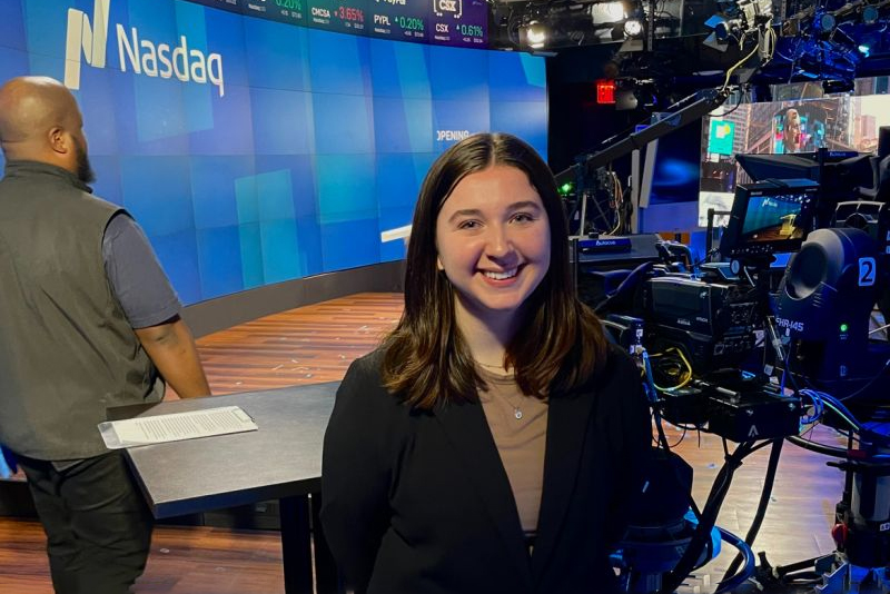Julia Fleming stands in a control room. A screen behind her says NASDAQ