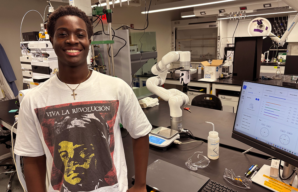 Diabene stands in the lab in front of a robotic arm.