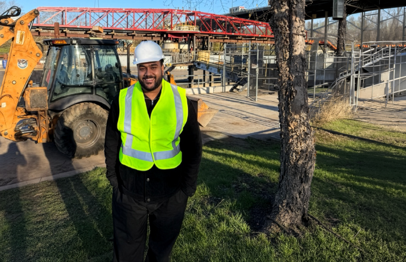 Arham stands in a yellow vest on a construction site.
