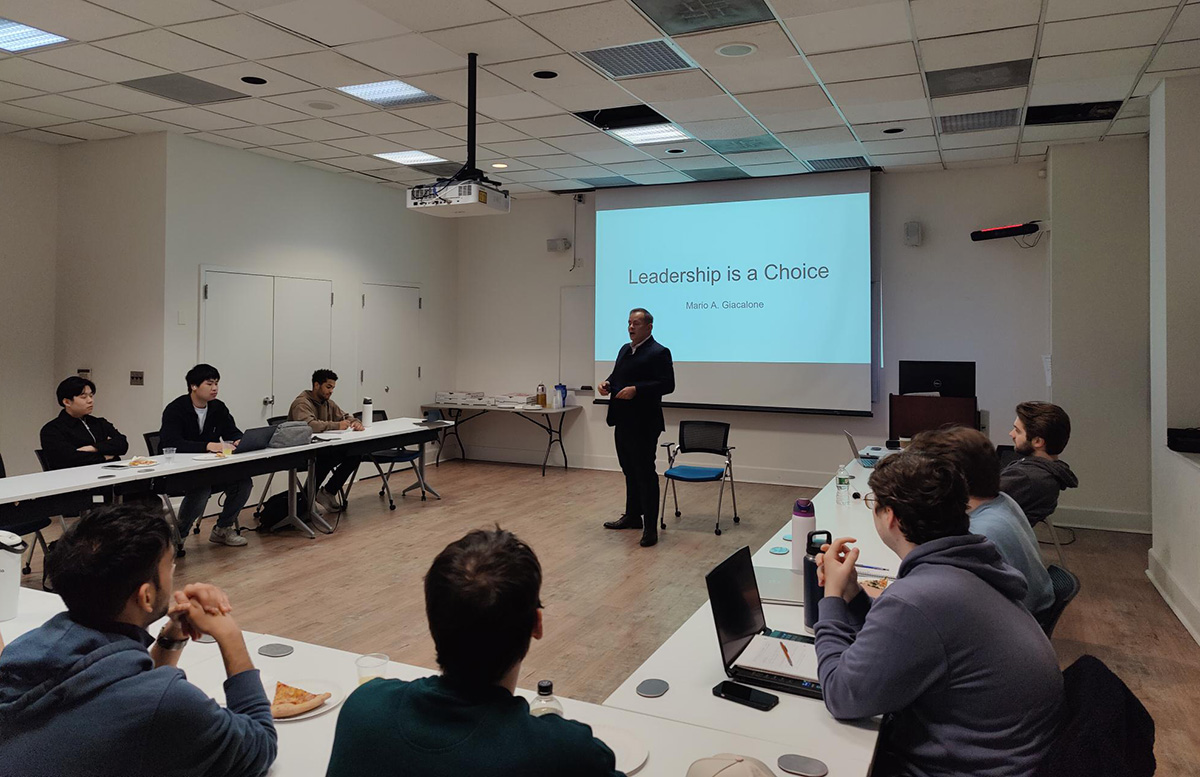 Giacalone stands in front of a u-shaped table, speaking to seated students