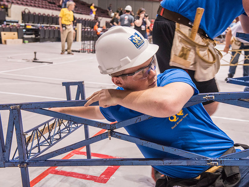 Student wearing hard hat building a steel bridge
