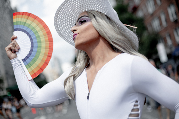 A fashionable individual in a white shirt and hat waving a rainbow fan.