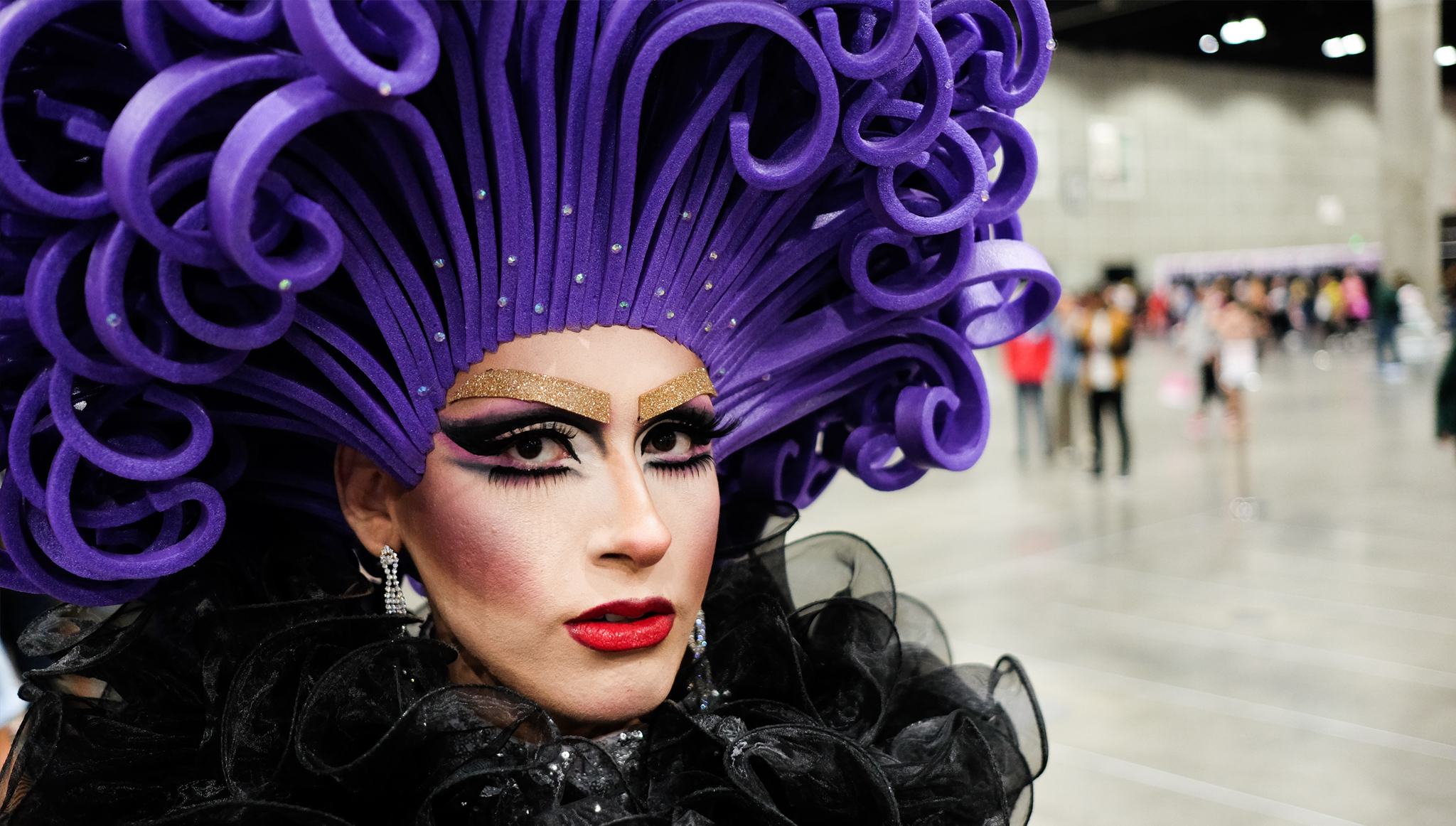 Drag queen in an ornate purple head dress with sparkles and glamorous makeup.