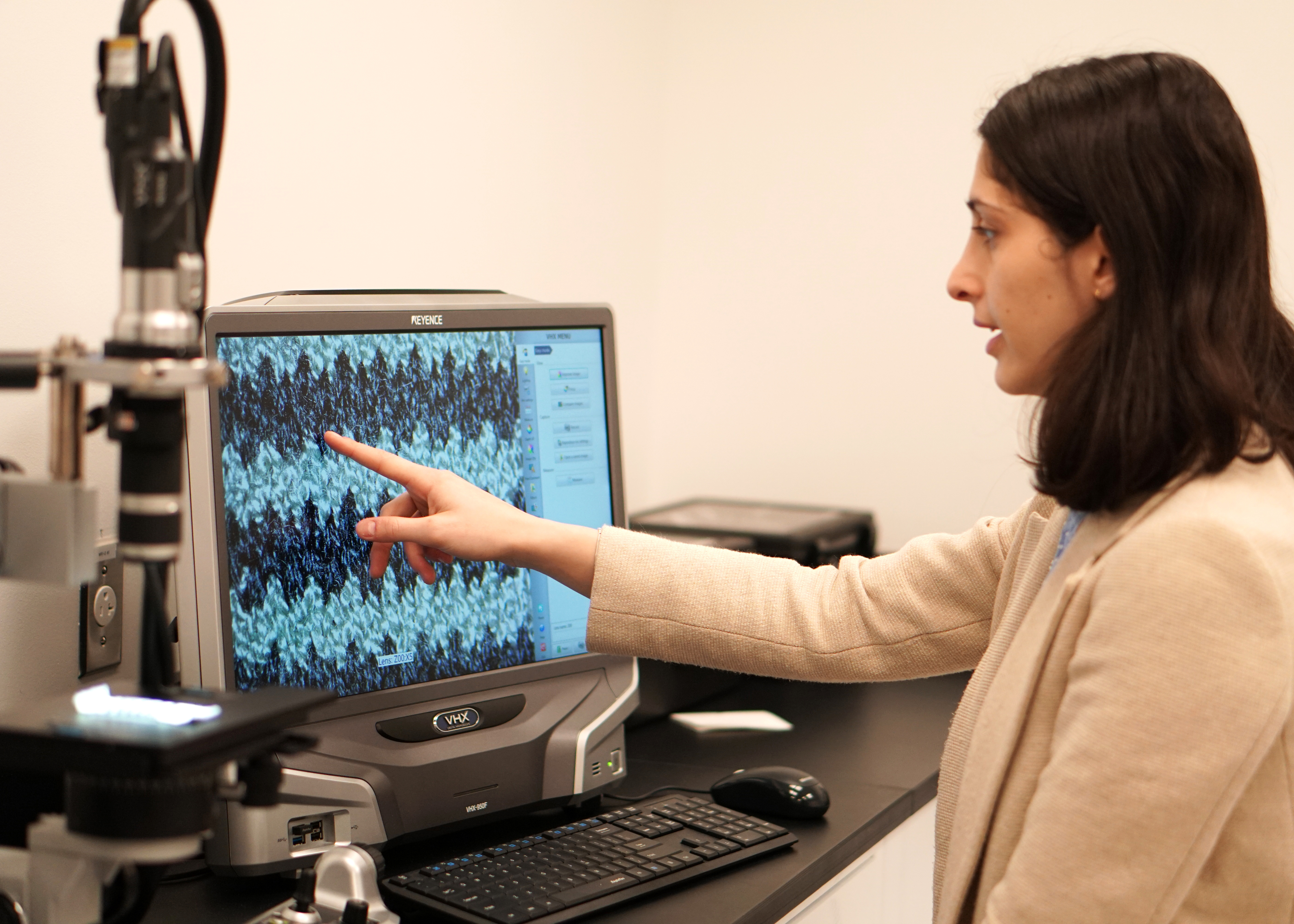 A person points at a computer screen displaying a close-up image of a textile