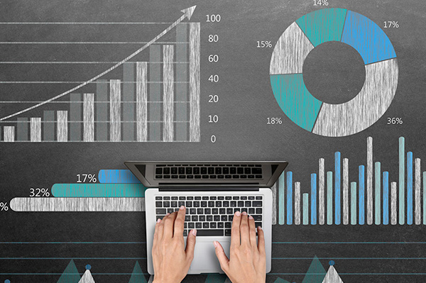 view of hands working on a laptop working atop a chalkboard covered with data visualizations