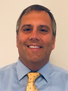 Headshot of smiling man in blue shirt and yellow tie
