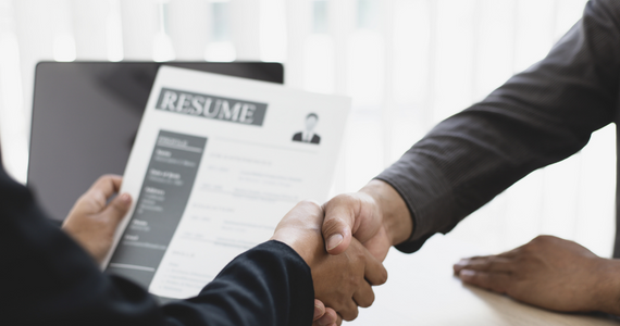 Person holding a resume in one hand and shaking hands with someone else, mixed race