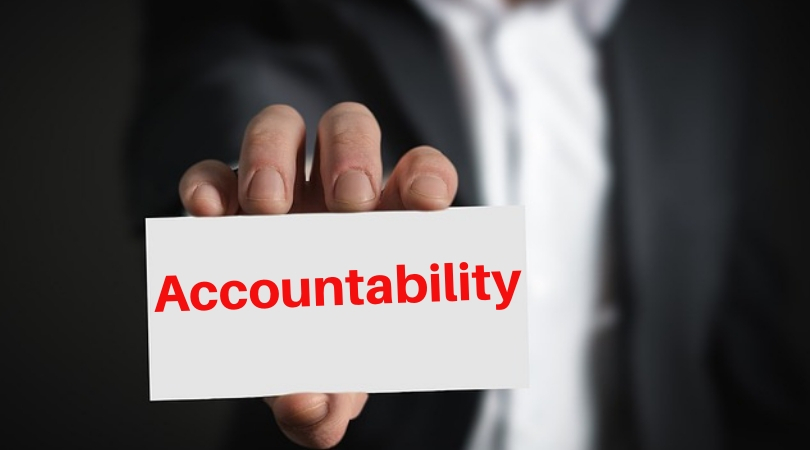 Image of a man in a suit holding a card. On the card in red bold font is written the word, "Accountability"