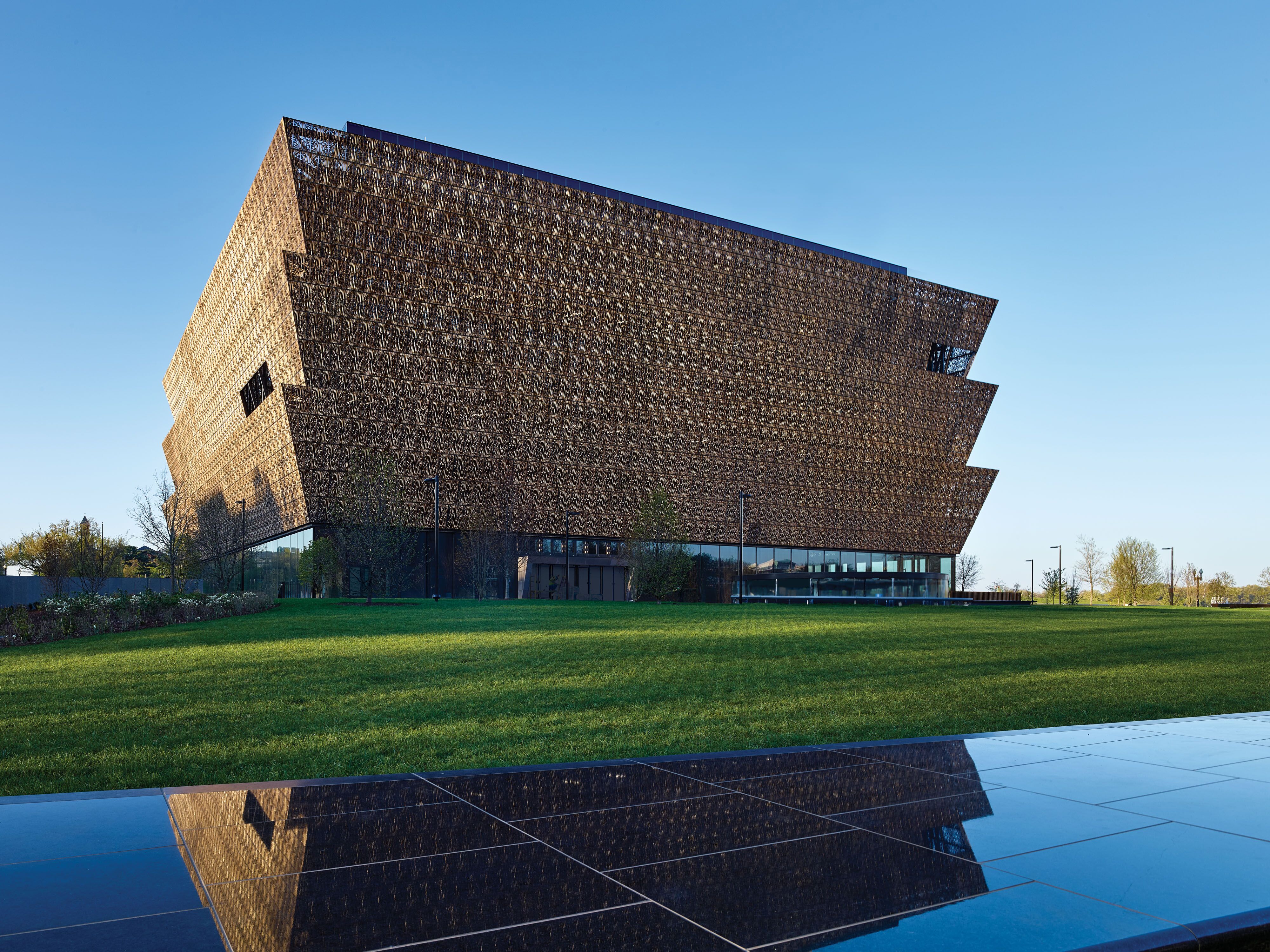 Image of the Museum of African American History and Culture. It is brown stricture depicting 3 levels with a reflection of it in the water.