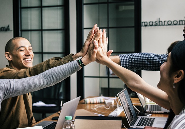 Image of a work team at a table high-fiving one another over their computers.