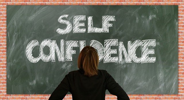 Image of a chalk board with a woman standing back-to, in front of it. THe words on the board read: Self-Confidence