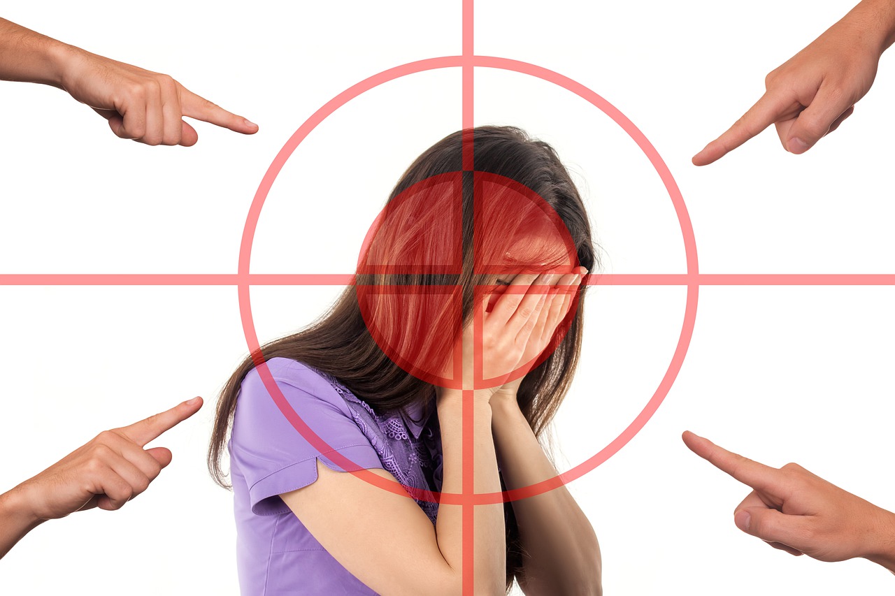 Image of a woman with target superimposed over her - she has her hand in her hands with a hand pointing at her in each corner to depict bullying