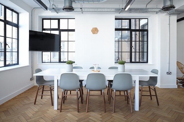 Image of an empty board room with white walls and chairs around a square table.