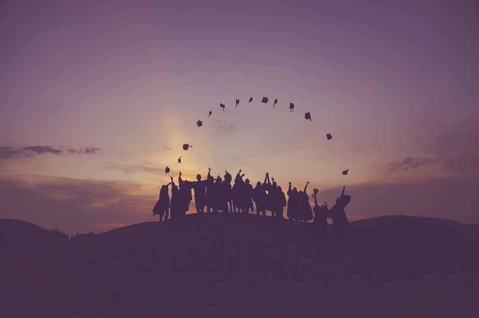 Image of graduate tossing up their caps at dawn with the sun just staring to rise behind them