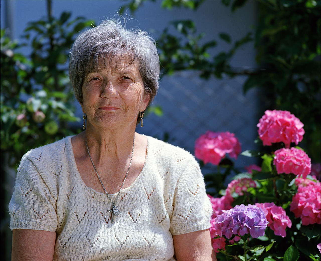 Picture of an older woman sitting outside with red flowers in the background.