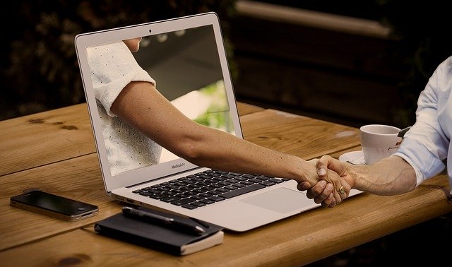 Image of a woman's arm coming out of a laptop computer and shaking hands with another.