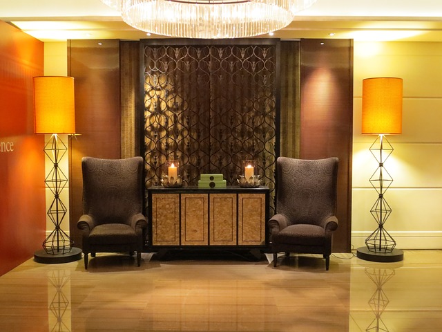 Image of an an empty small hotel lobby with a table in front of a draped window flanked by two tall chairs