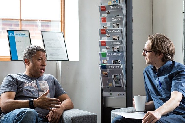 Image of two men, one black, one white, talking with one another in an office setting, but in casual clothes