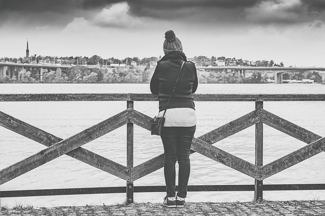 Black & White image of a young woman standing on a bridge looking out across the water in the winter time