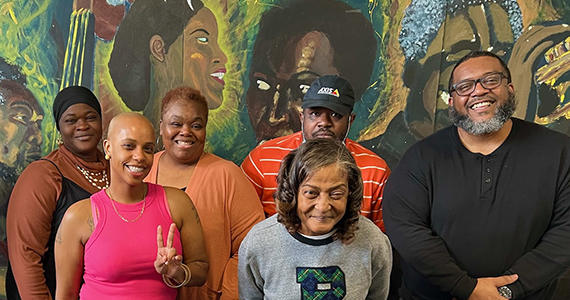 Six Black adults standing in front of colorful mural