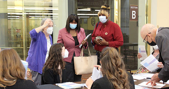 Three women standing as others organize papers on a table