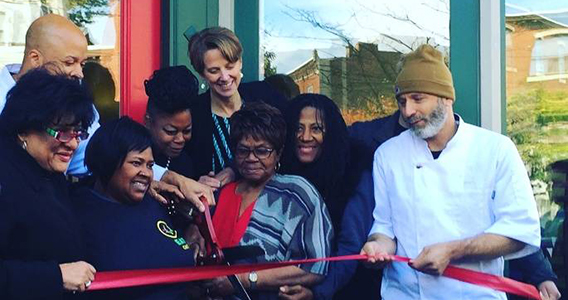Group of people cutting a ribbon in front of the EAT Cafe