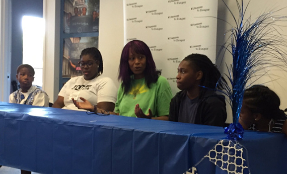 Three children and two adults speaking on a panel