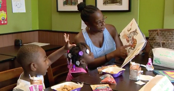 Woman reading a book to two children who are eating
