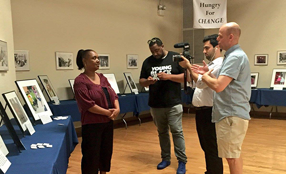 Member of Witnesses to Hunger being interviewed by cameramen at a photo exhibit