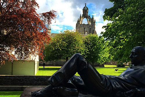 Statue of a reclining figure in the foreground and a cathedral-like building in the background on the campus of University of Aberdeen.