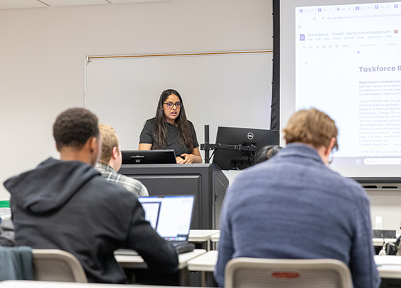 Speaker addresses a classroom full of students and faculty during an AI policy simulation.