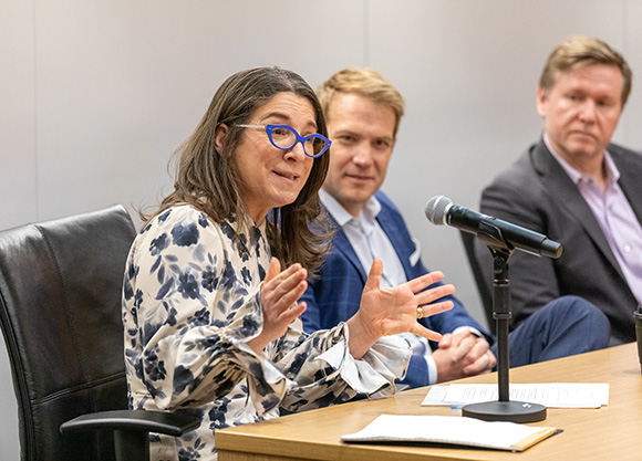 Close-up of a panelist addressing an audience while two other panelists look on.