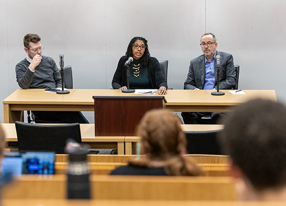 Three professors sit at a table facing an audience during a panel discussion.