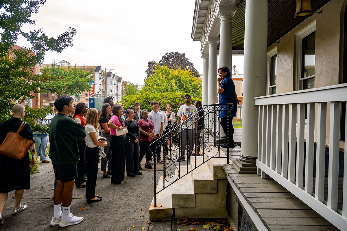 Undergraduate students gather around the porch of the Dornsife Center while a professor speaks.