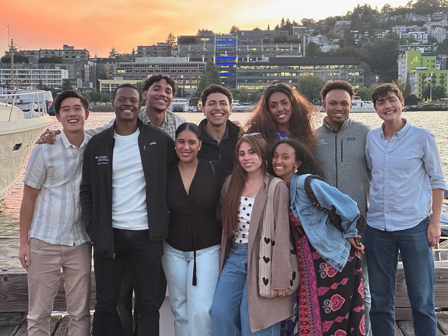 10 students stand with water in background and buildings in distance