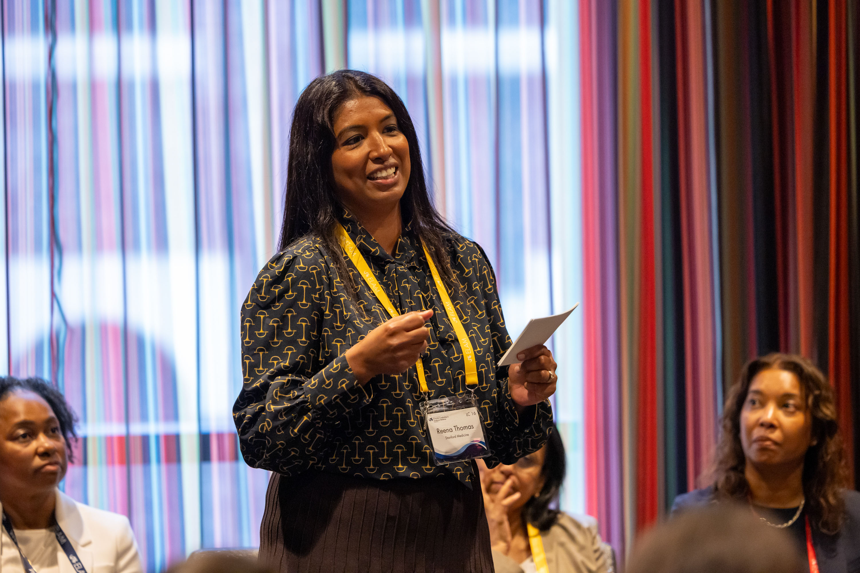 woman standing in center as other, seated, listen engaged