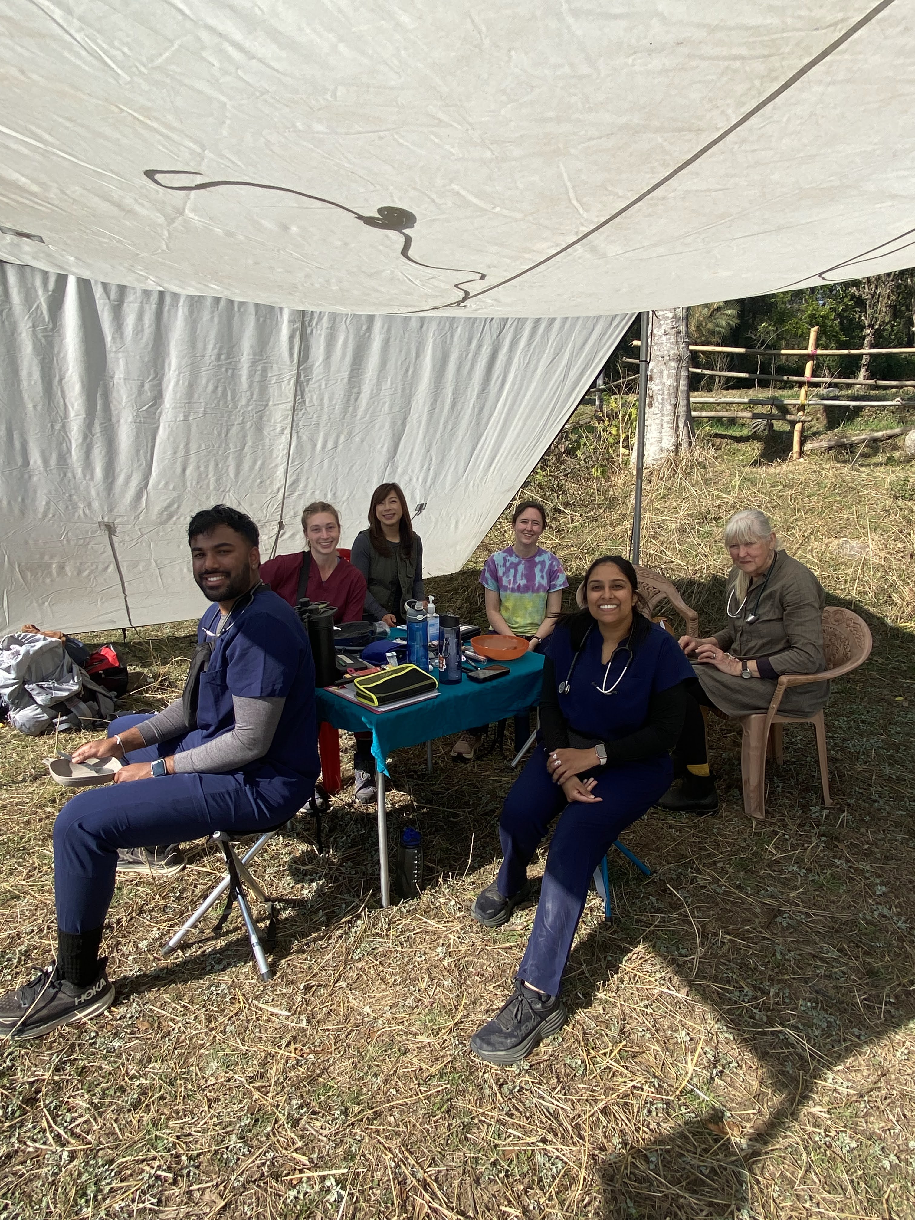 six people sit around a table in an open shade tent