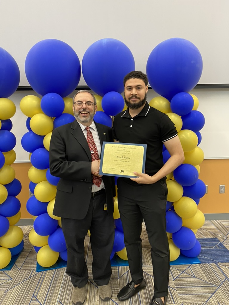 2 men holding certificate with balloons in the background